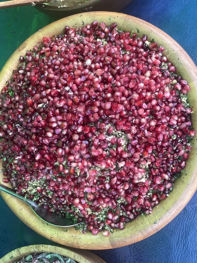 Large wooden bowl of pomegranate seeds, bulgur and chopped herbs with a serving spoon