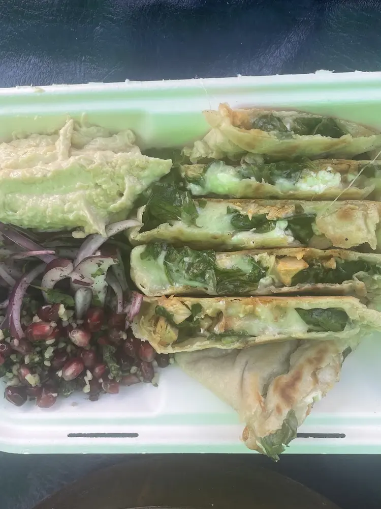 Takeaway box holding sliced spinach and cheese gözleme with hummus, sumac onions and pomegranate salad