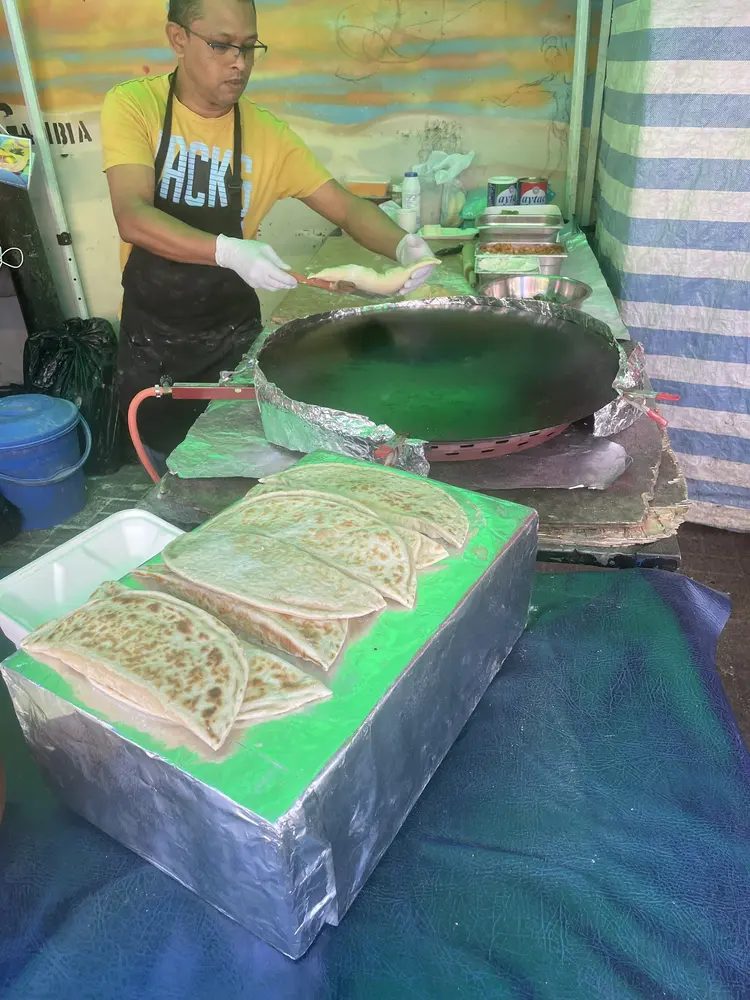 Cook in an apron folding gözleme dough beside the large round iron griddle, cooked gözleme stacked in front